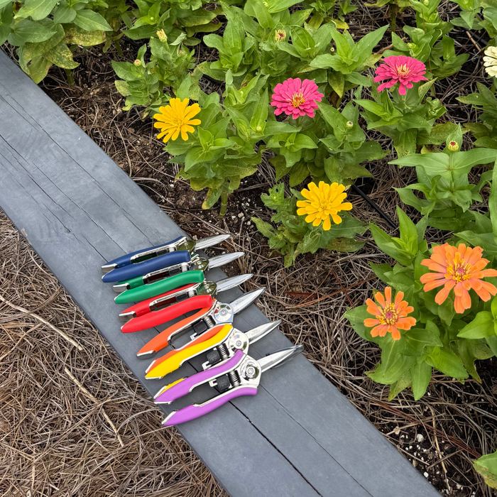 Set of colorful pruning shears on a wooden surface with flowers in the background