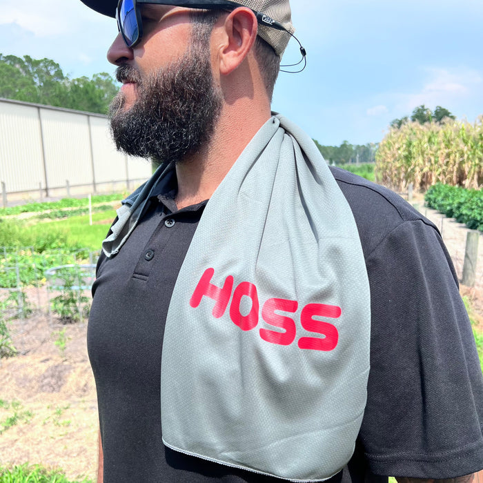 Man wearing a gray 'HOSS' branded towel over his shoulder outdoors.