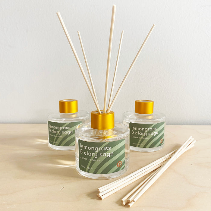 Three glass aroma diffusers with lemongrass and clary sage scent, featuring wooden reeds and gold caps, on a wooden surface.