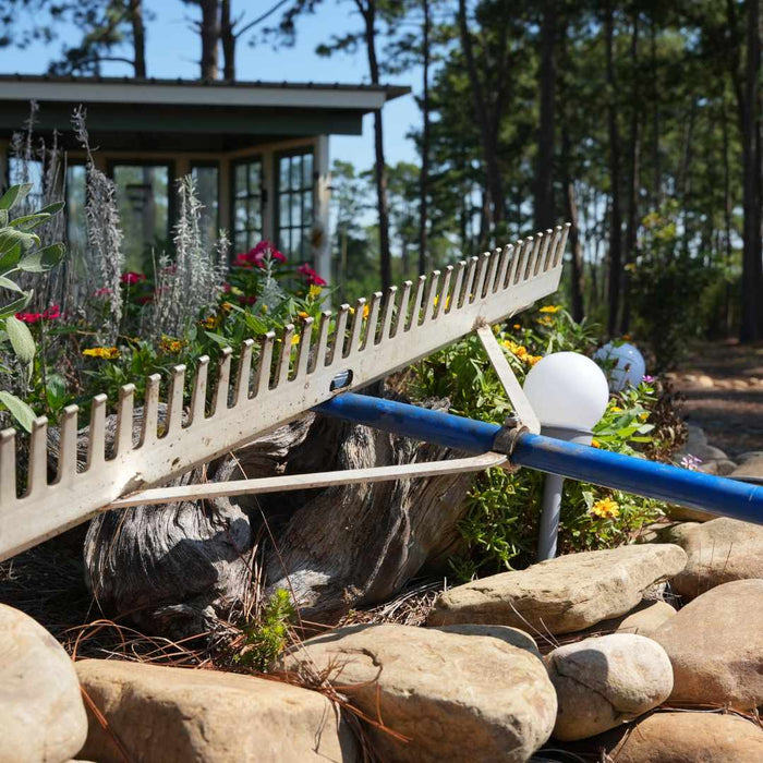 Garden rake leaning against a stone wall with a garden and house in the background