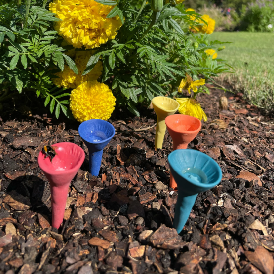 Colorful , handmade ceramic funnels on mulch with yellow flowers in the background