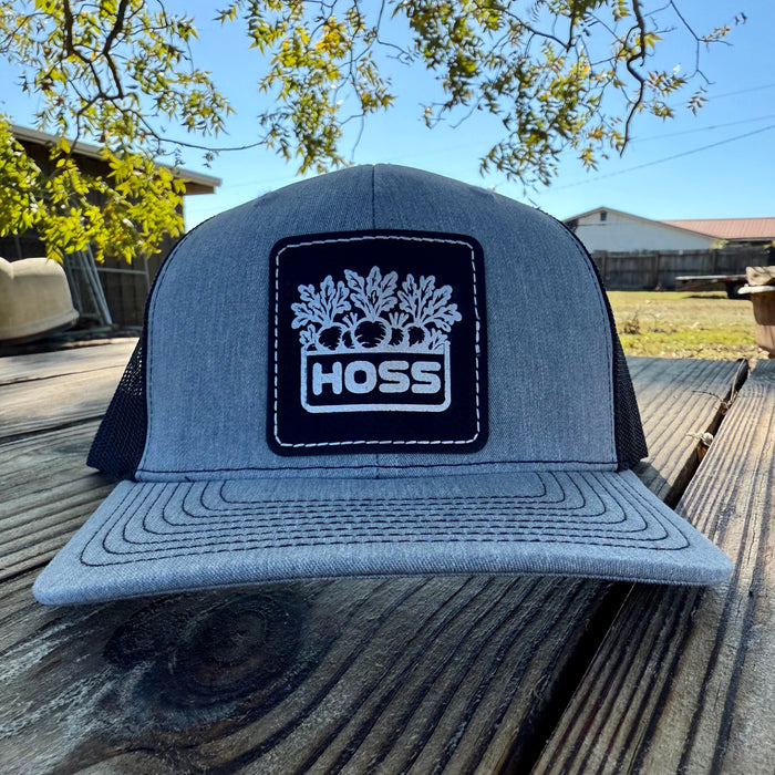 Gray trucker hat with 'HOSS' logo on a wooden surface outdoors