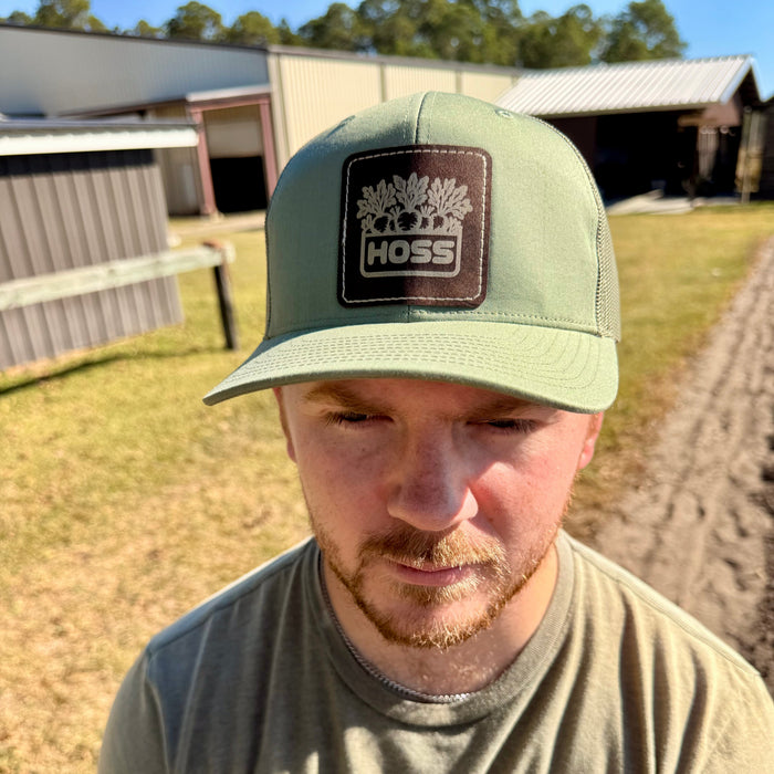 Man wearing a green cap with a Hoss logo in an outdoor setting