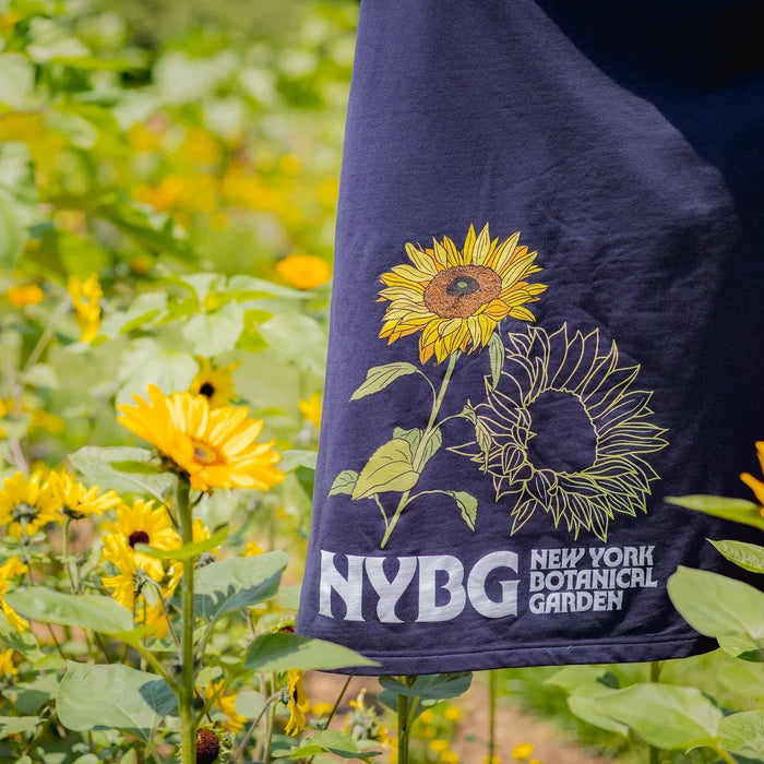 Navy blue towel with sunflower design and 'NYBG New York Botanical Garden' text held in front of a sunflower field.